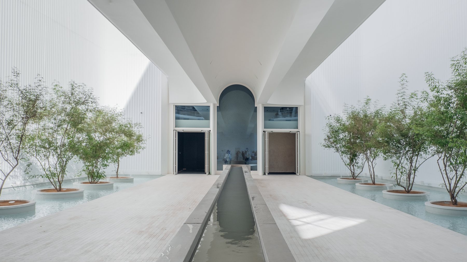 Symmetrical white courtyard with olive trees and a reflecting channel